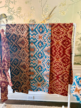 Load image into Gallery viewer, Three patterned scarves hanging on a rack against a decorative wall.