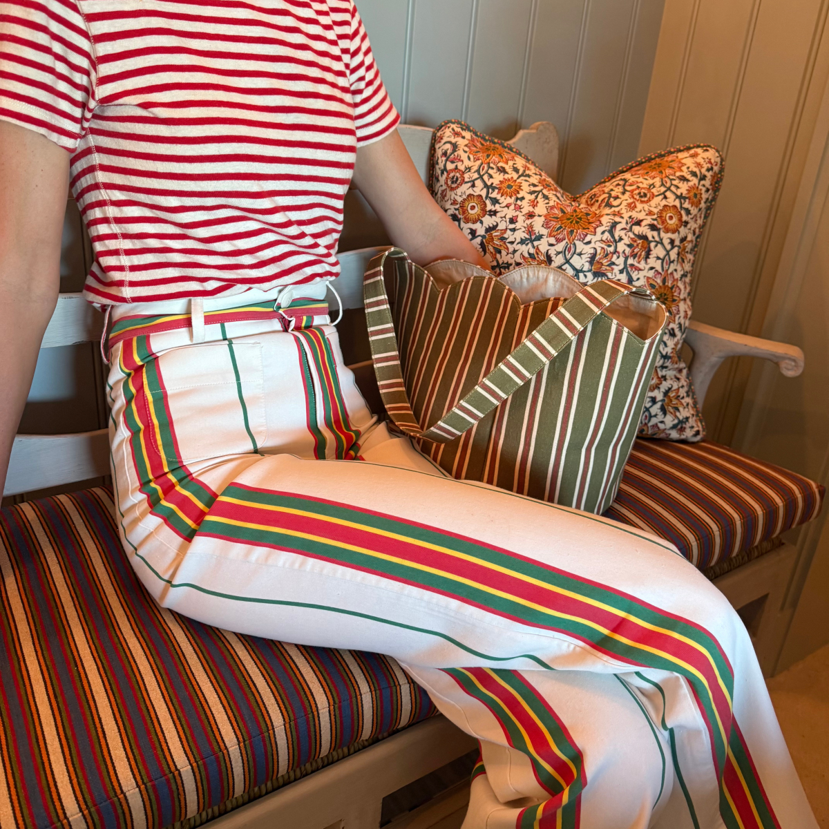 Person wearing a red and white striped shirt and colorful striped pants sitting on a bench with patterned cushions.