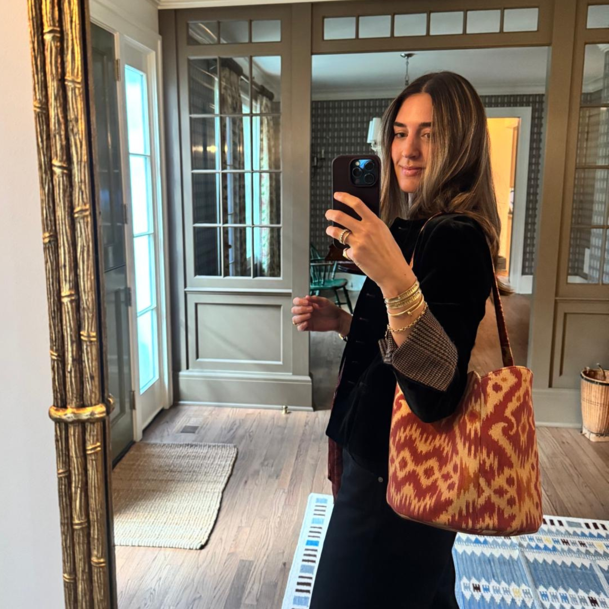 Woman taking a mirror selfie in a home setting with a patterned bag.