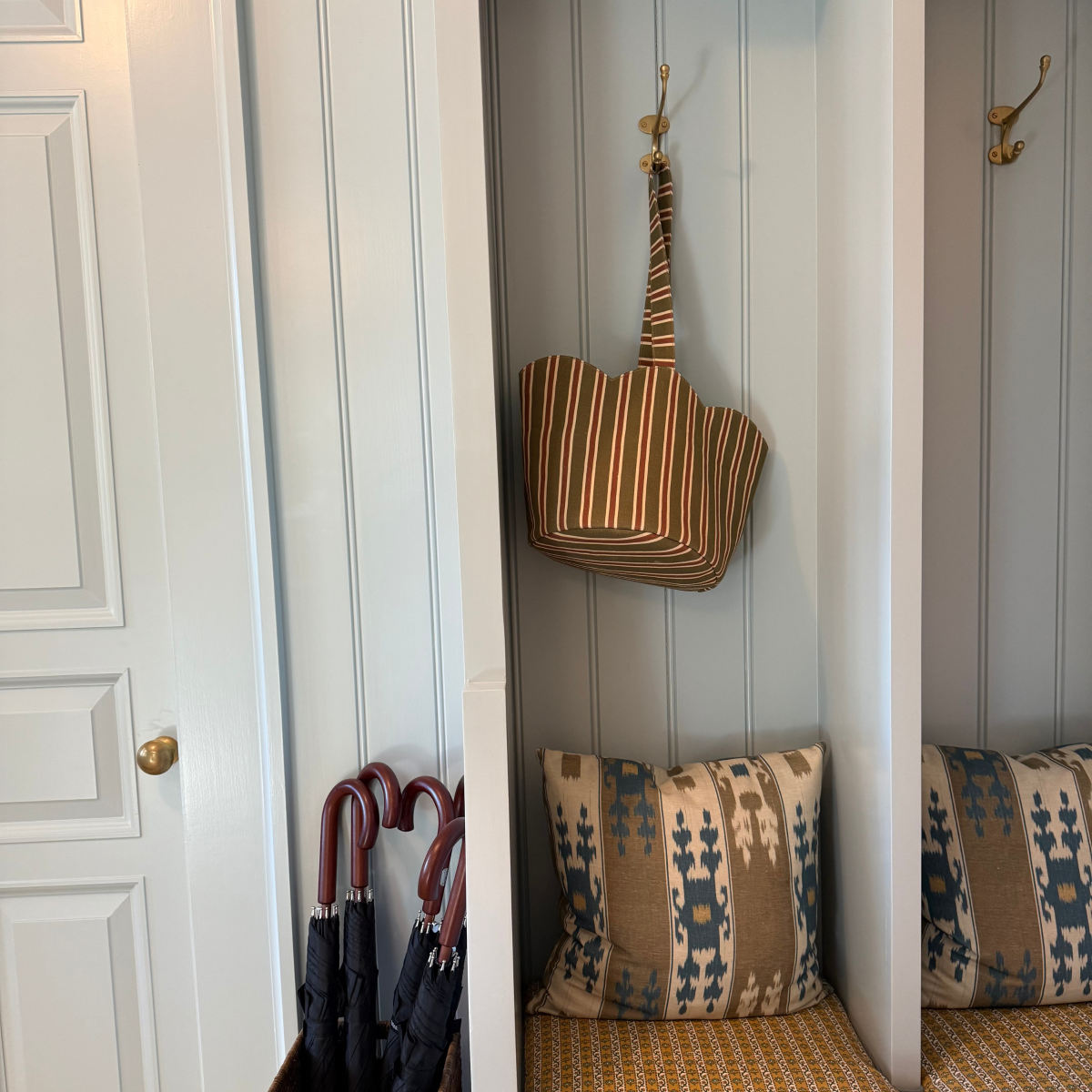 Striped bag hanging on a hook above patterned cushions in a room with white walls and a door.