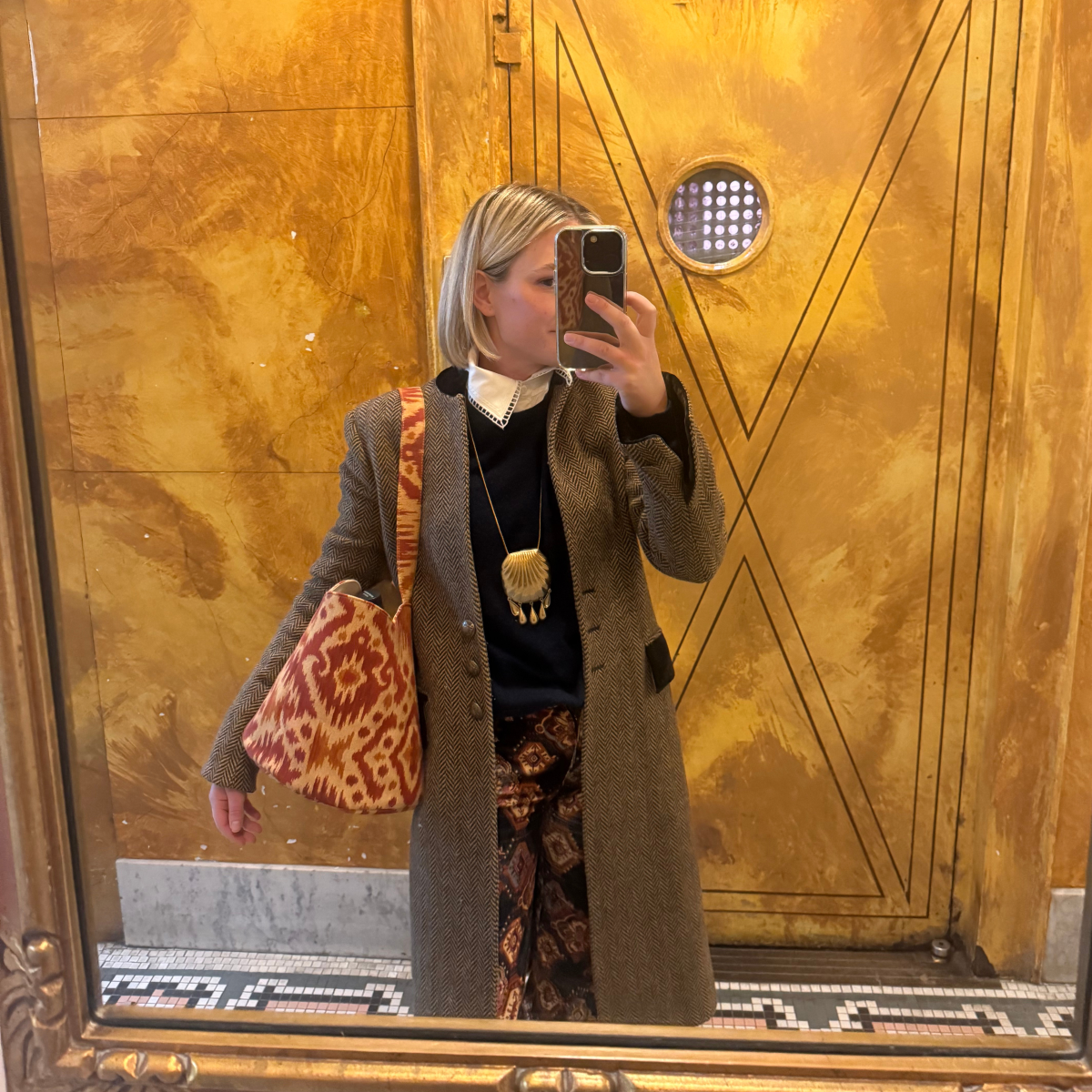 Person taking a mirror selfie in front of a gold door with geometric patterns.