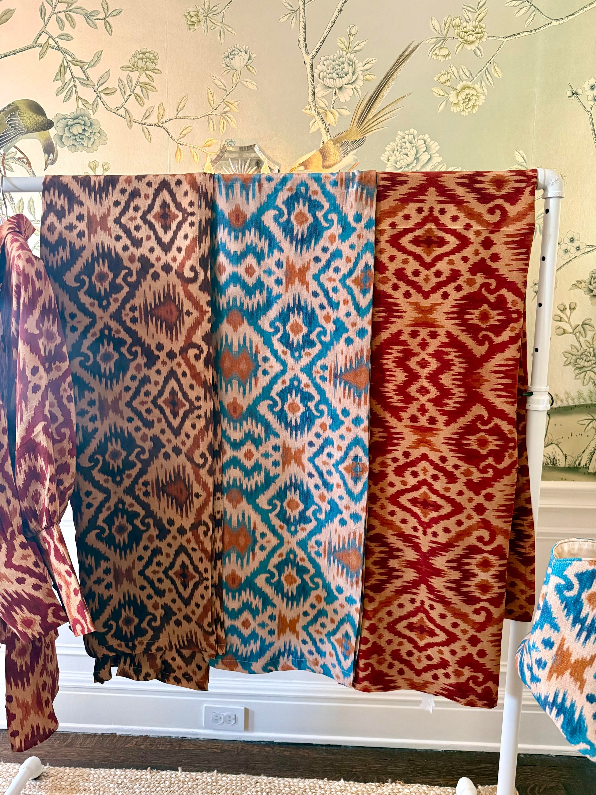 Three patterned scarves hanging on a rack against a decorative wall.