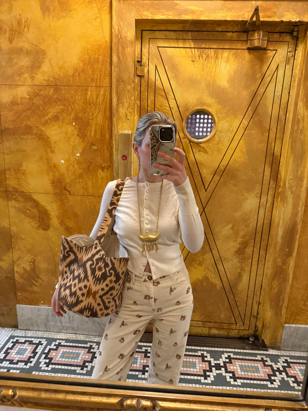 Person taking a mirror selfie in front of a gold door with intricate designs.